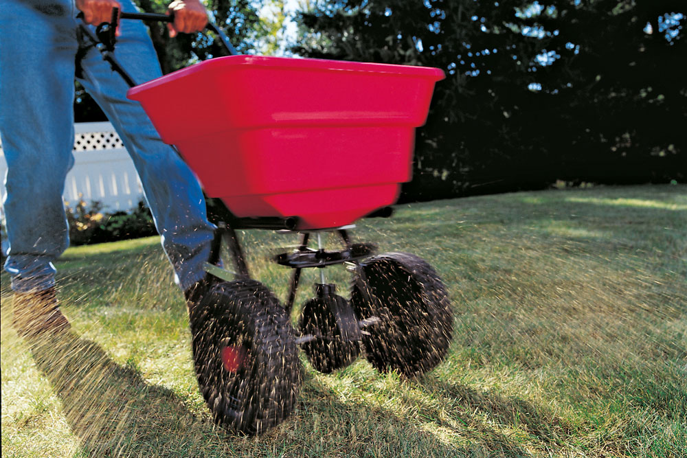 A person sowing grass seed using a drop spreader