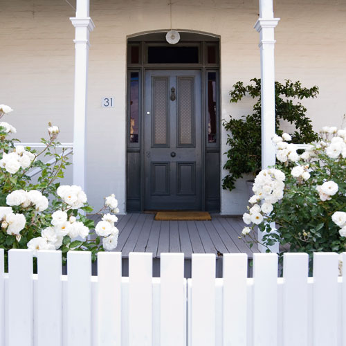 a home with white fence and black door, the entrance of a home after it is had been revamped, 
